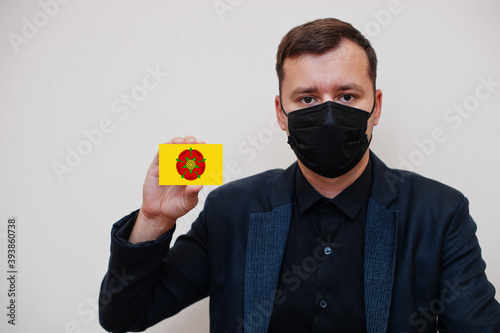Man wear black formal and protect face mask, hold Lancashire flag card isolated on white background. United Kingdom counties of England coronavirus Covid concept. photo