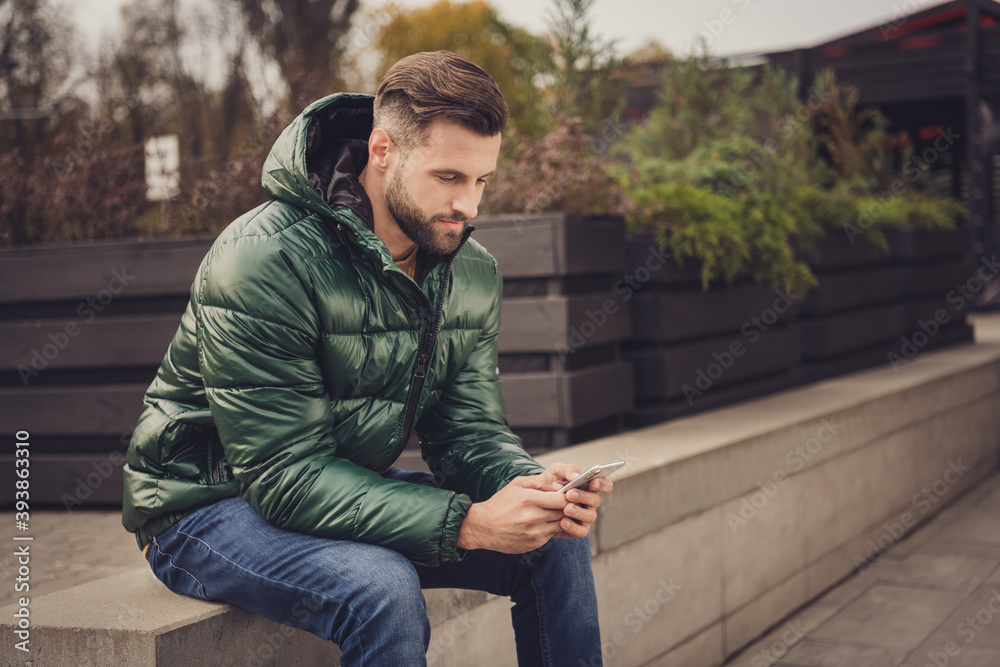 Profile side photo of handsome attractive young man wear green windbreaker typing modern device outside city street