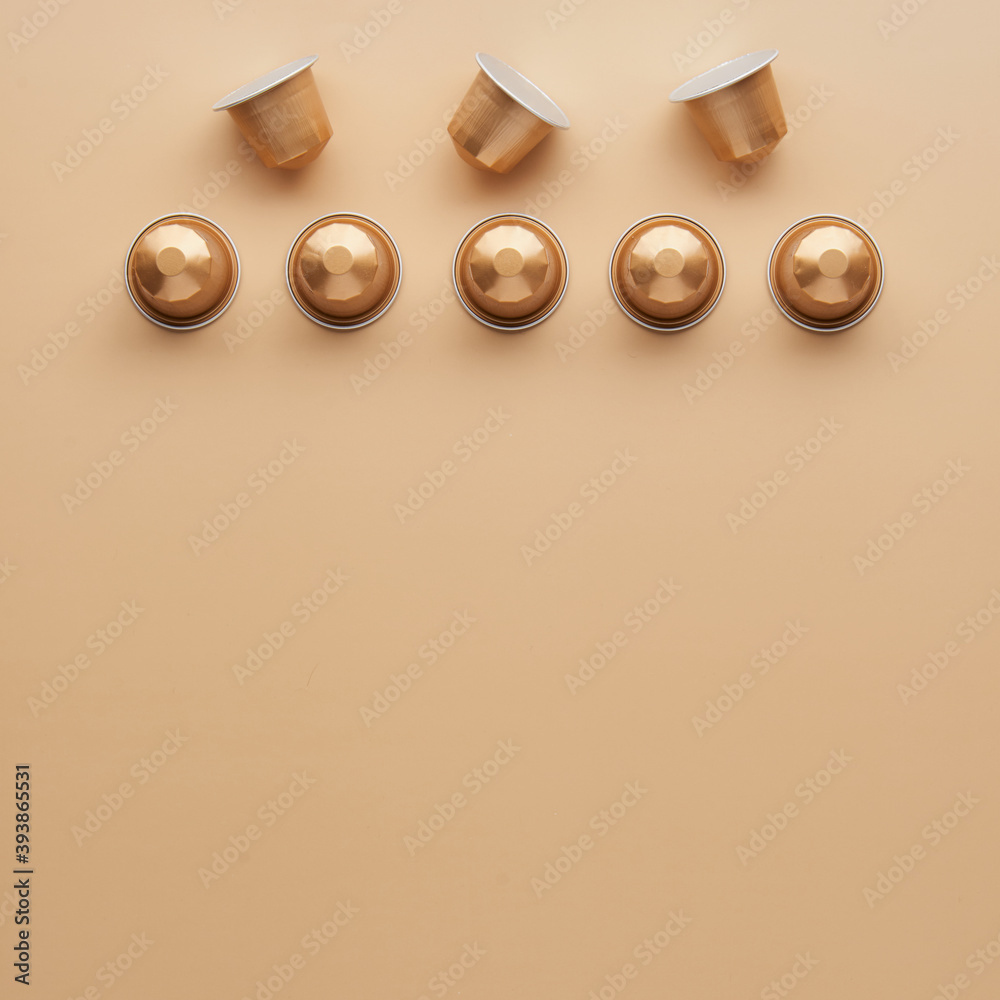 Caffeine, hot drinks and objects concept - close up of golden capsules or pods for coffee mashine on beige background. Top view with space for text. Flat lay..
