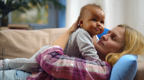 Smiling caucasian mother holding adopted mixed-race baby at home photo