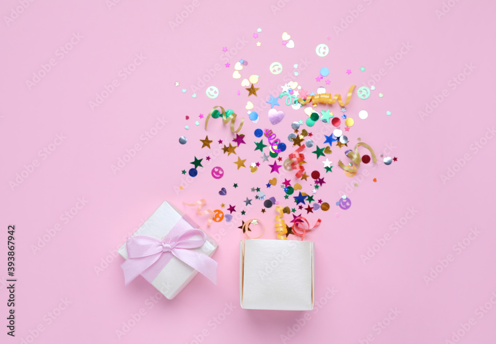 Shiny colorful confetti bursting out of box on pink background, top view