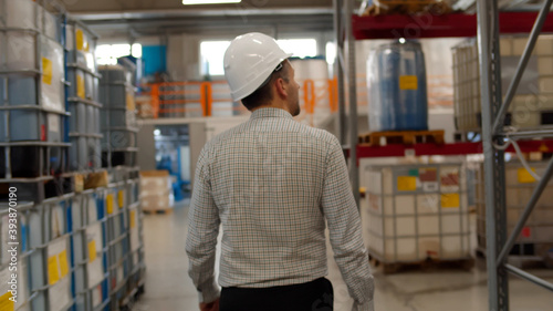 Back view of male manager in helmet walking in industrial warehouse