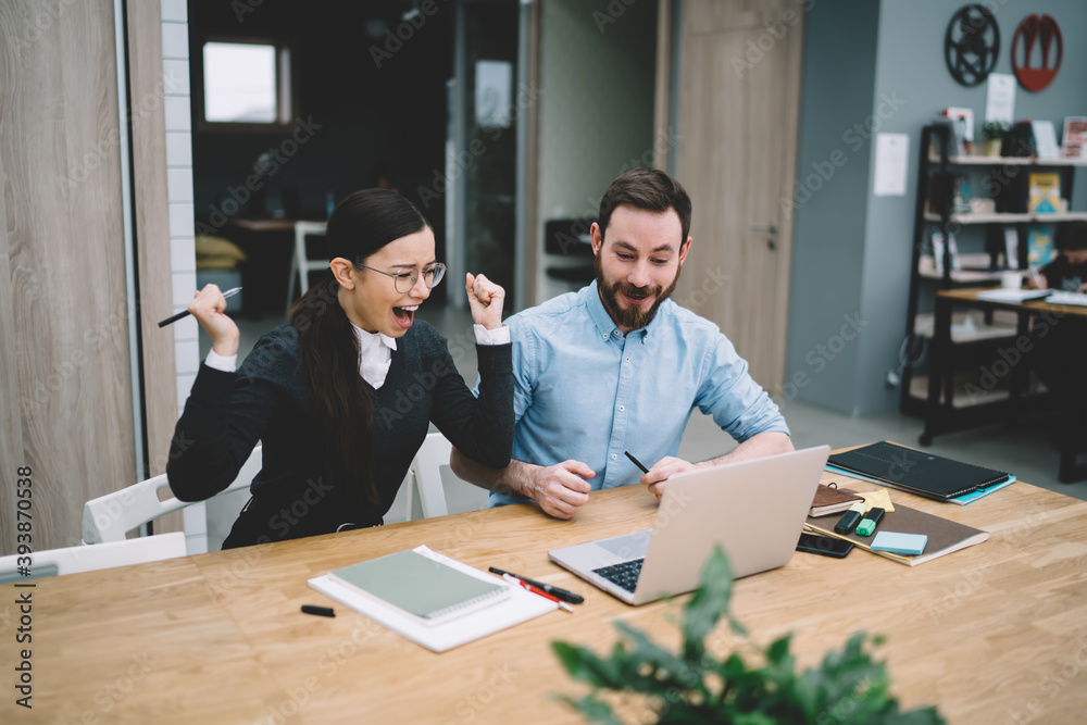 Woman raising hands screaming with joy near man in office Woman raising hands screaming with joy near man in office
