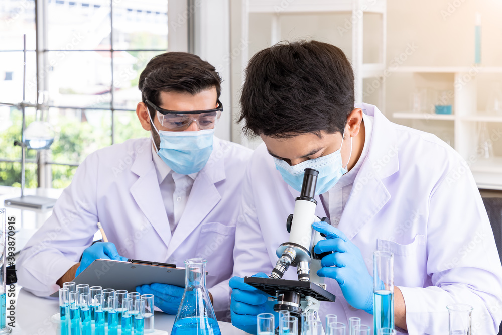 Two male Asian and Arab researcher scientists working in laboratory, conducting study biohazard substance with scientific equipment and microscope