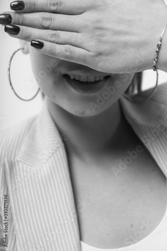 Beautiful laughing young woman covering her eyes with her hands over a light studio background