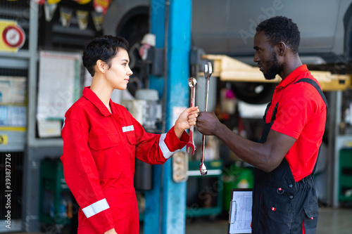 Portrait Auto mechanic with wrench in hand. stranglehold. car repair black man and caucasian woman inspector in red uniform © NVB Stocker