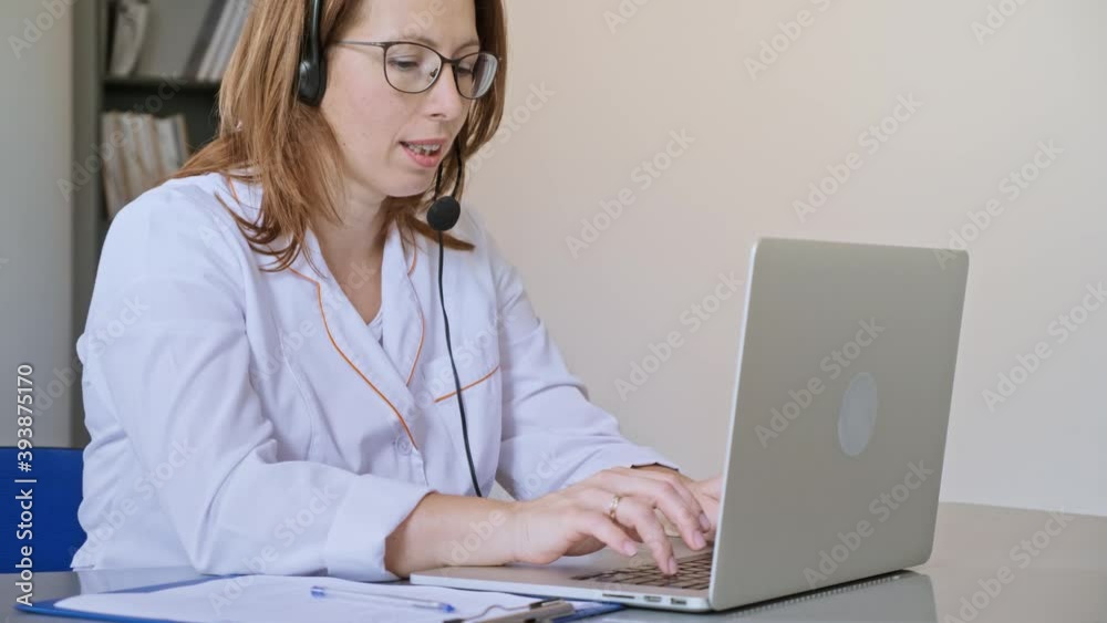 Friendly Female Doctor in White Medical Coat With Headphones Making Conference Call on Laptop.Remote Consulting Patient Online From Healthcare Hospital. Telemedicine. Friendly Female Doctor in White Medical Coat With Headphones Making Conference Call on Laptop.Remote Consulting Patient Online From Healthcare Hospital. Telemedicine.