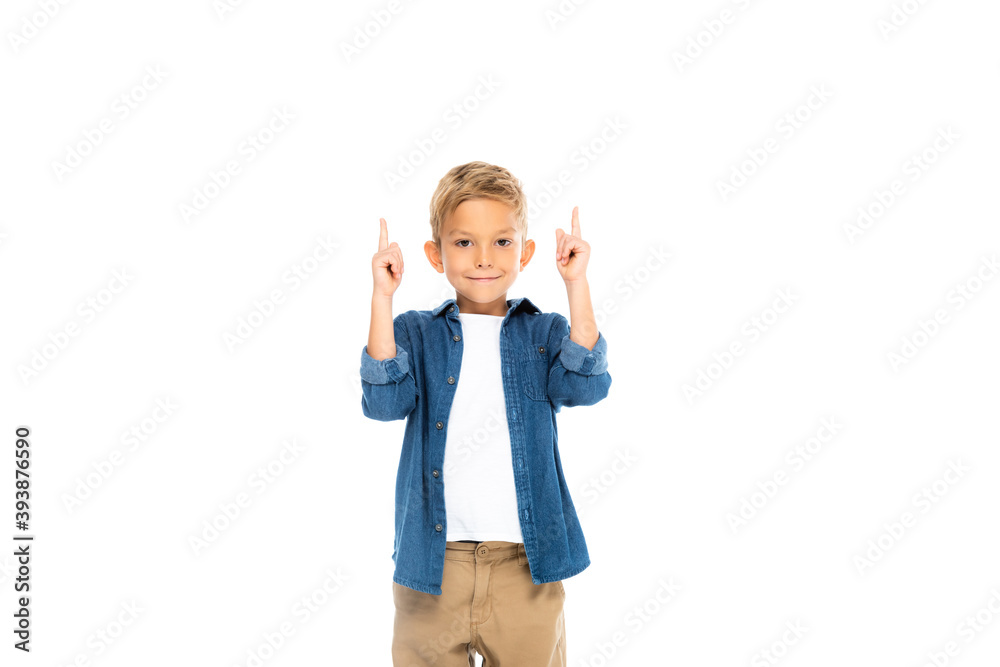 Positive boy looking at camera while pointing up with fingers isolated on white