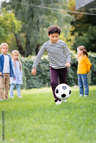 Asian boy playing football near friends in park at background