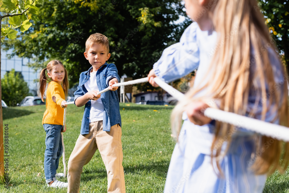 Boy pulling rope while playing tug of war with friends on blurred foreground in park Boy pulling rope while playing tug of war with friends on blurred foreground in park