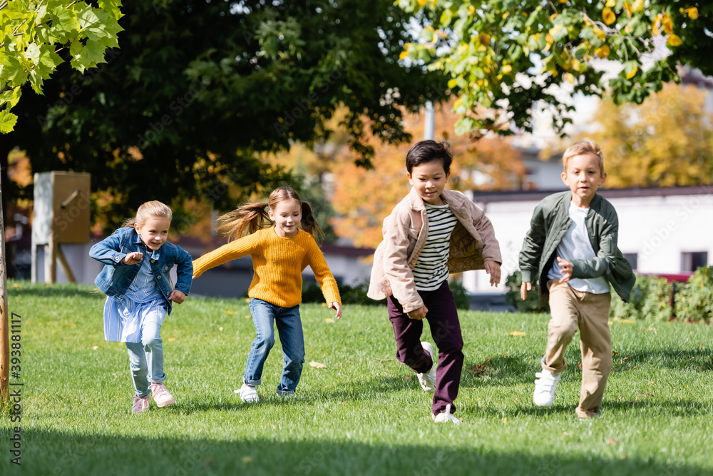 Smiling multiethnic children running on grass in park Smiling multiethnic children running on grass in park