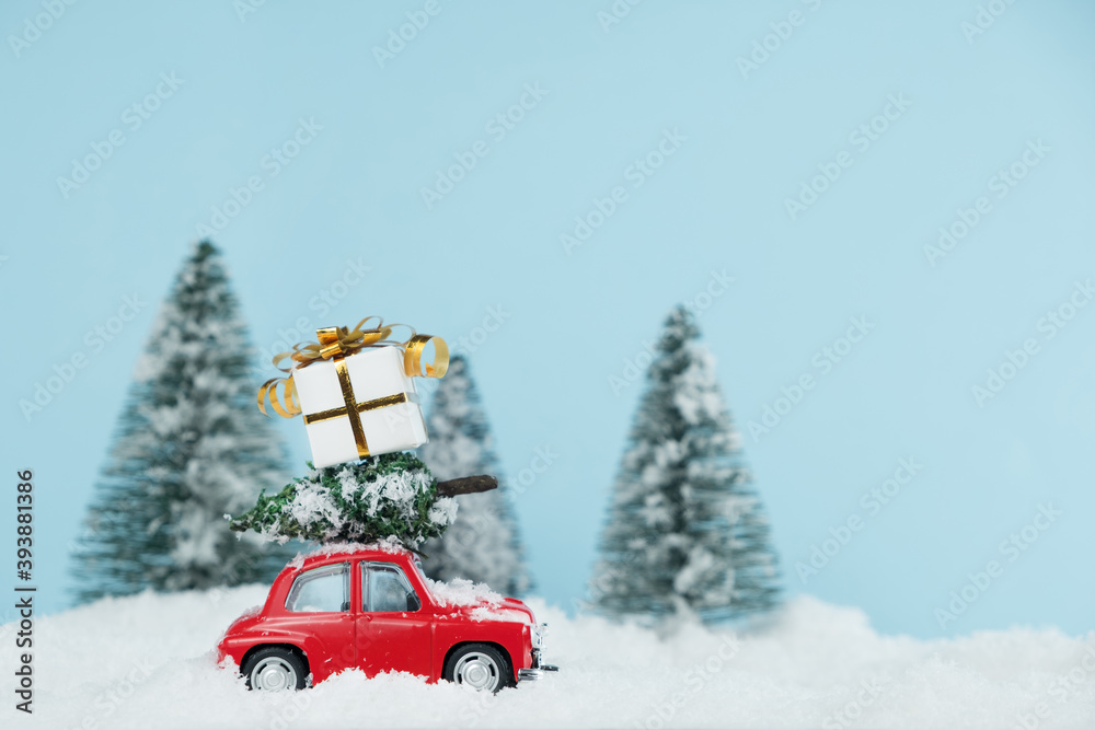 Christmas red car with a gift box in a snowy pine forest. Space for text. Happy New Year card concept Christmas red car with a gift box in a snowy pine forest. Space for text. Happy New Year card concept