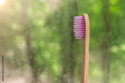 one bamboo toothbrushe close-up on nature background. green bokeh. biodegradable materials. Eco-friendly plastic replacement. pink bristles