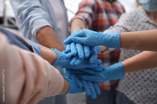 Group of people in blue medical gloves stacking hands indoors, closeup © New Africa