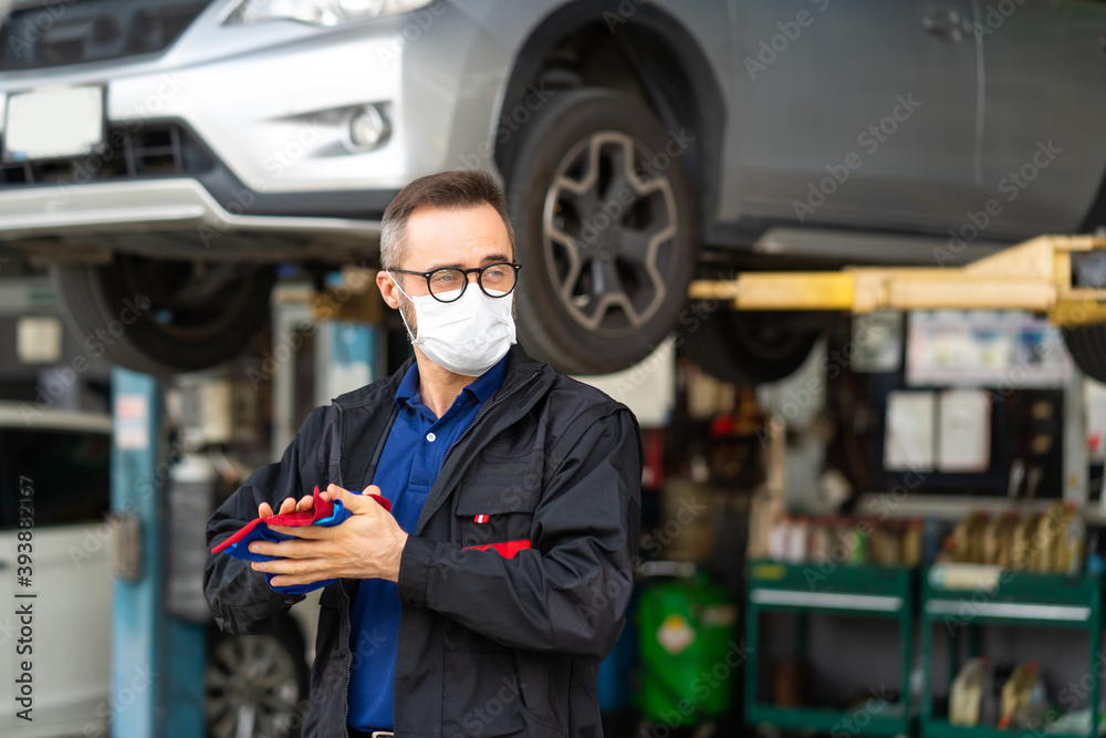 Portrait of caucasian man Cleaning Hands With Cloth and wearing medical face mask protection coronavirus.. Expertise mechanic working in automobile repair garage. Portrait of caucasian man Cleaning Hands With Cloth and wearing medical face mask protection coronavirus.. Expertise mechanic working in automobile repair garage.