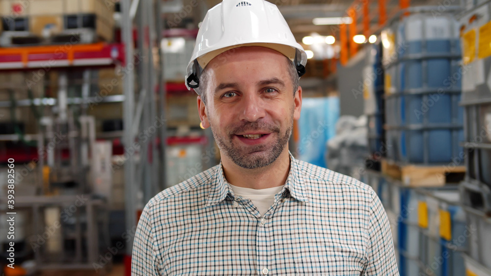 Portrait of industrial worker in safety hardhat smiling at camera in warehouse Portrait of industrial worker in safety hardhat smiling at camera in warehouse