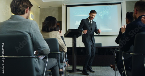 Caucasian male business coach finishing his performance at the conference and going away cheerfully while people applauding.