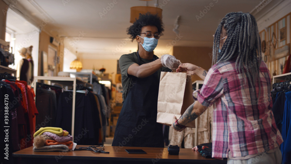 Young woman in safety mask purchasing in clothes store