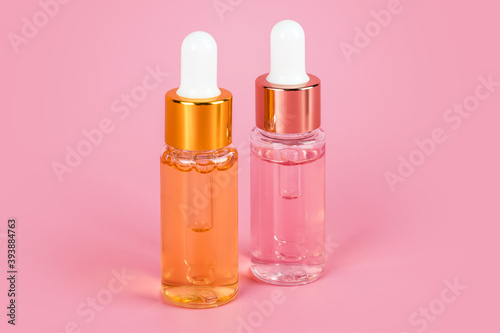 Two skin care essence oil dropper glass bottles on pink background. Hydrating serum, vitamins for skin. Anti aging serum with collagen and peptides in glass bottle with dropper. Aesthetic, minimalism.