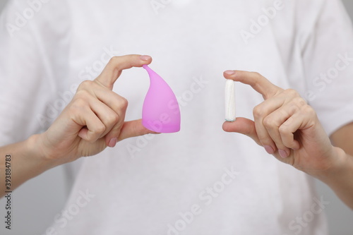 Close up view of young woman making choice between menstrual cup and tampon, on white background. Gynecology concept photo