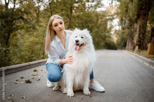 woman in white shirt is hugging her white dog samoyed outdoors in the park.