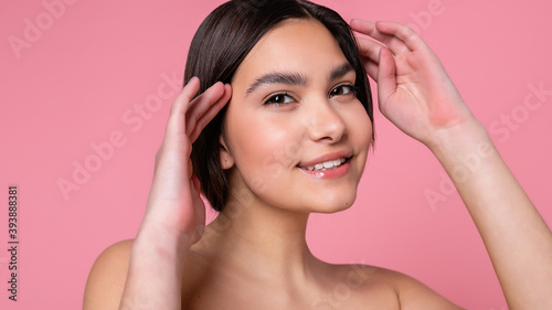 Close up face of beautiful young woman with clean perfect skin. Portrait of beauty model with natural nude make up. Spa, skin care and wellness. Pink peach coral background. 16:9 panoramic format.