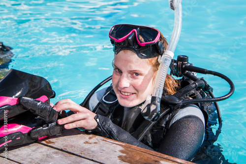 Scuba dive training in a pool, diver looking at the camera putting her fins on the deck smiling.