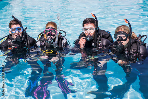 Scuba dive training in a pool with a group of students looking at the camera with their regulators in their mouths.