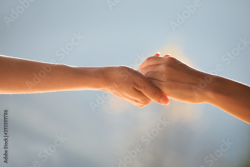 Two hands supporting each other, holding each other against the gentle blue natural background. © Ann Stryzhekin