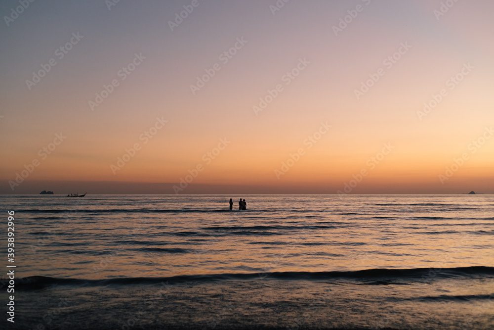 3 men boys swimmers stand in the water during sunset in the sea indian ocean silhouetted by the backlight sun with small waves