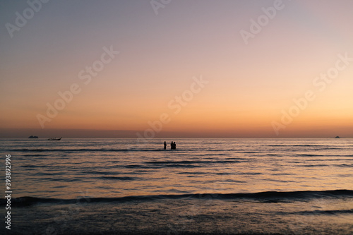 3 men boys swimmers stand in the water during sunset in the sea indian ocean silhouetted by the backlight sun with small waves