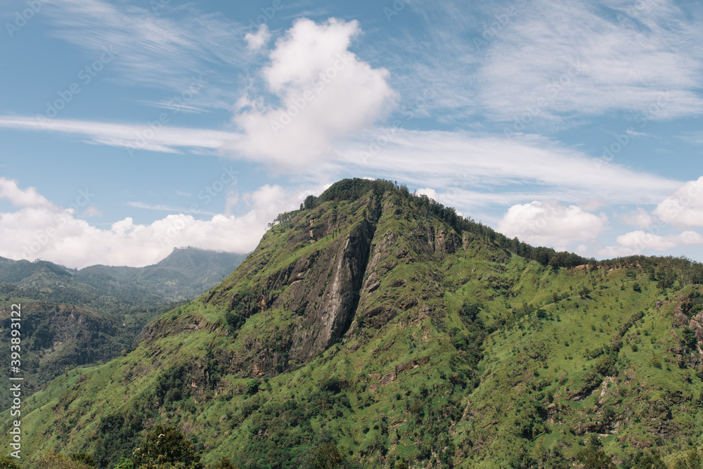 elevated view of little adam's peak in ella, sri lanka during summer, showing the hill mountain covered in trees and soil with a gap in the middle and blue skys