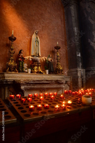 Fotografie Photo of votive candles in a chapel placed in front of religios statue
