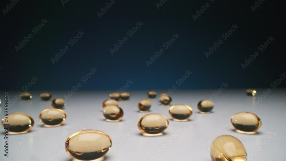 Conceptual macro dolly shot of spilled cod liver oil pills on white table at dark background in studio Conceptual macro dolly shot of spilled cod liver oil pills on white table at dark background in studio