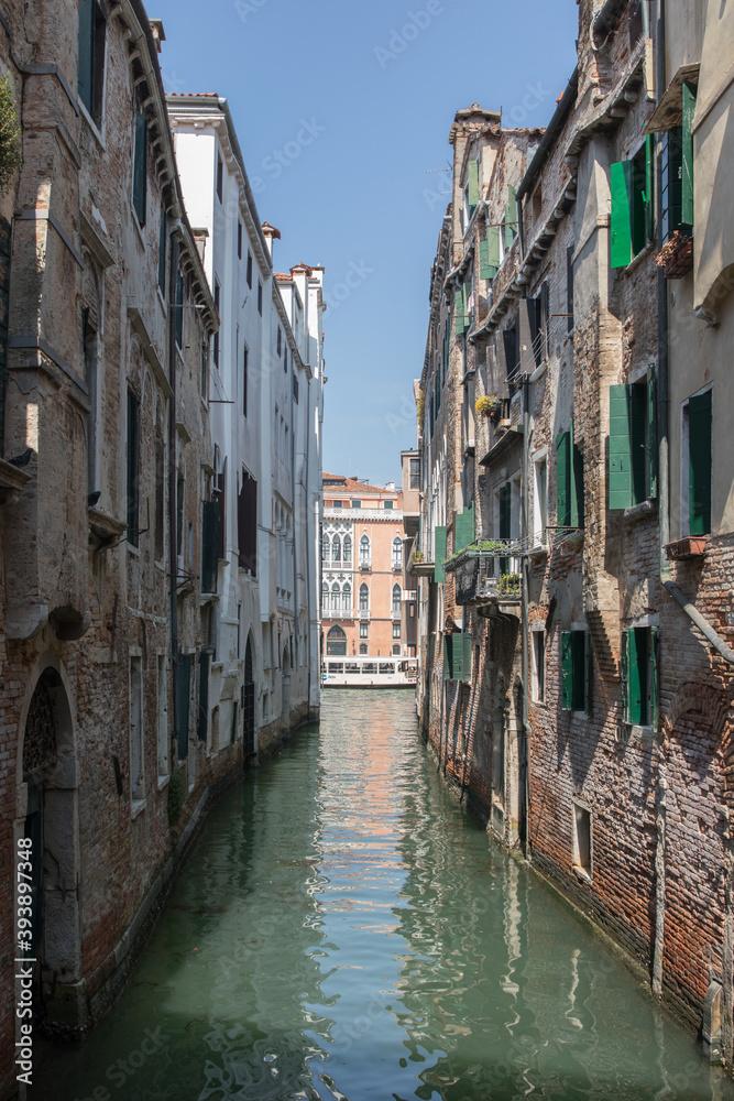 river canal view from bridge boat in venice italy during summer with buildings to each side colourful water blue skies green windows