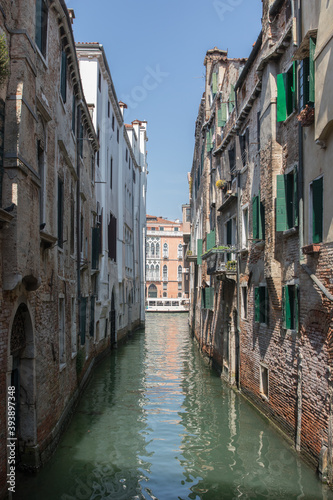 river canal view from bridge boat in venice italy during summer with buildings to each side colourful water blue skies green windows © Adam
