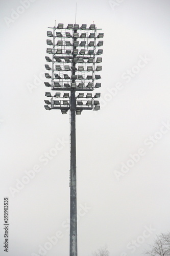 Stadium floodlight with metal pole, lighting mast, tower with floodlights in the sports stadium against the white sky.