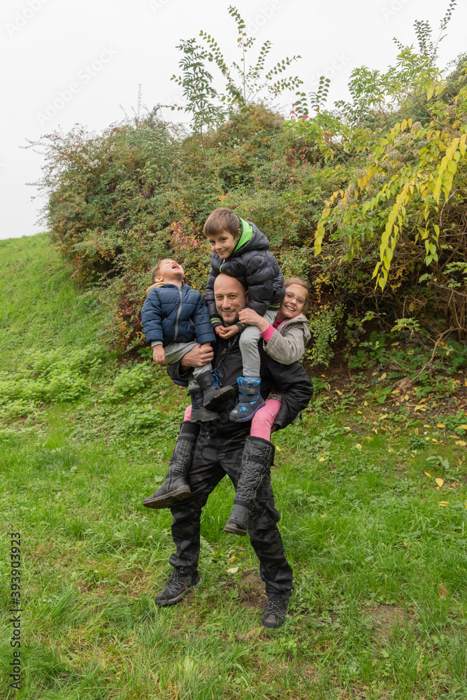 The father is carrying three children. Father carrying childs piggyback. The father plays with the childrens on an autumn day