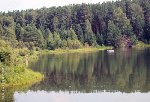 Fototapeta Naklejka Na Ścianę i Meble -  Summer landscape: a forest lake, the reflection of trees in the water, people in a boat and a mother with a child.