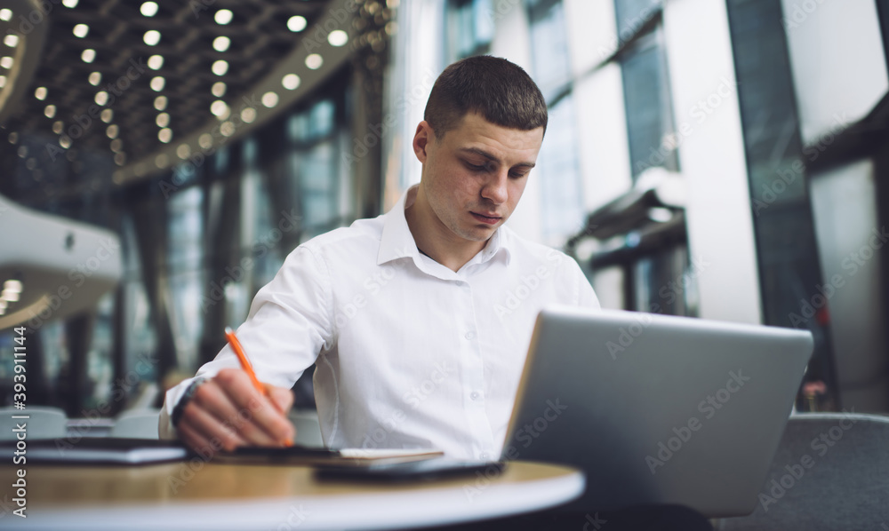 Thoughtful businessman taking note while using laptop in cafe