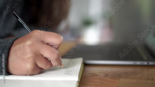A person in the house working on her laptop and taking notes on a paper notebook. Focus following the hand movement.