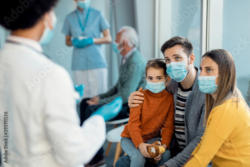 Young family with protective face masks talking to a doctor at medical clinic.