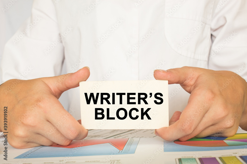 a man in the office holds a card with text WRITER'S BLOCK . business concept a man in the office holds a card with text WRITER'S BLOCK . business concept