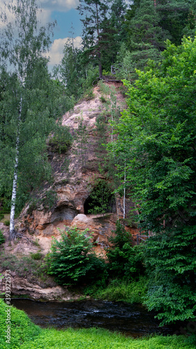 Sandstone Caves in Ligatne, Latvia. View to Cave Rock Lustuzis (Lustūzis) on the Bank of Ligatne River. Caves With Old Wooden Doors.