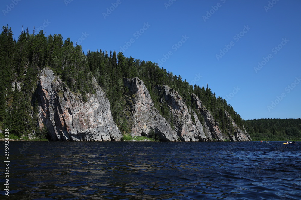 Unique natural landscape mountains lake.Rocks with a forest on top.A huge cliff in the water.A stone boulder.Concept of summer tourist active vacation.Kayaks with people on the horizon in the wild