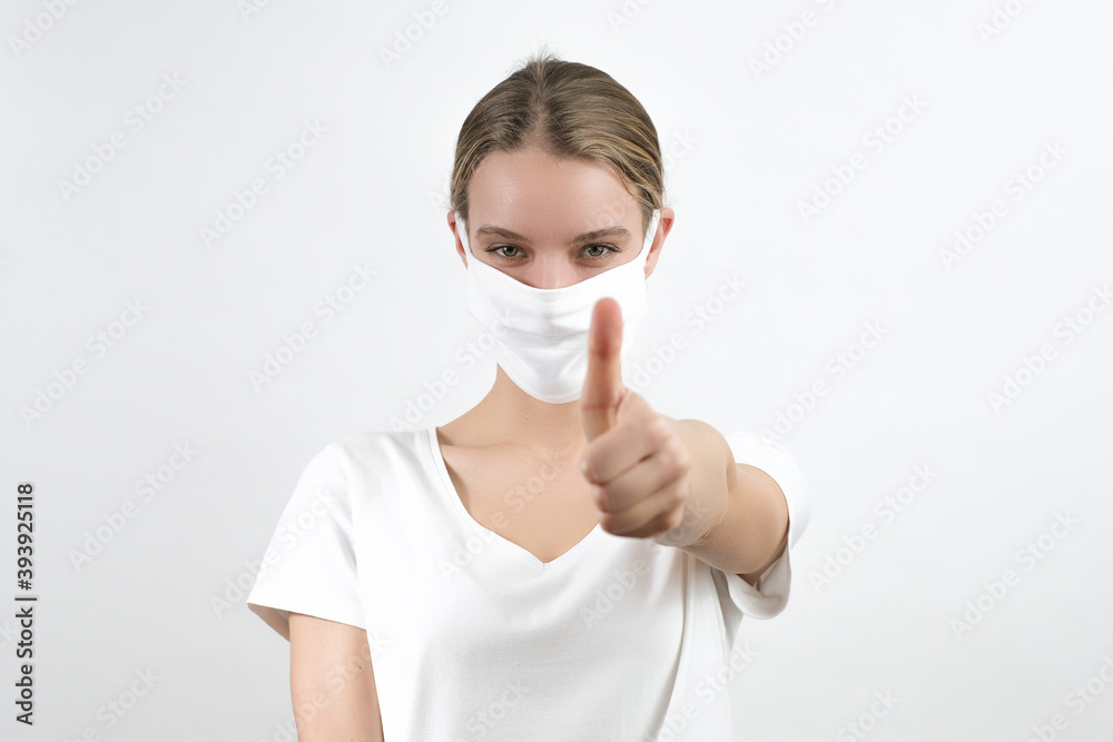 Young white woman wearing protection face mask showing in front of her thumb. Virus, covid-19, coronavirus. Young white woman wearing protection face mask showing in front of her thumb. Virus, covid-19, coronavirus.