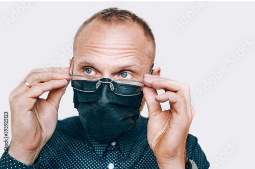 Portrait of man taking off glasses in black facial mask during a COVID-19 world pandemic looking at camera. Virus self-protection and vision health concept image.