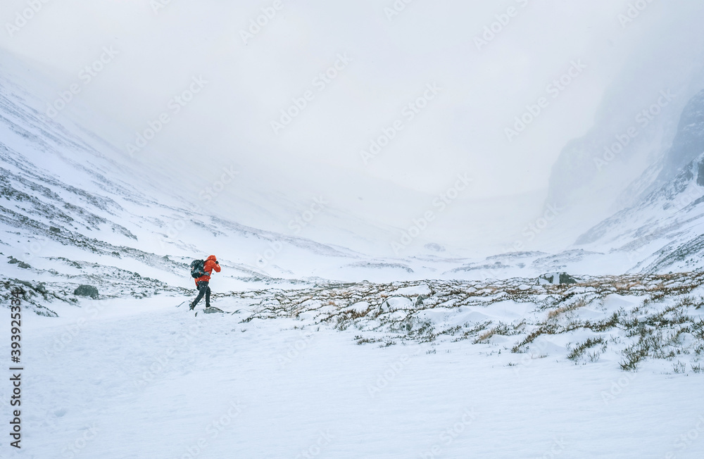 Alone mountaineer has a solo winter Ben Nevis 1345m summit approaching in high mountains on windy snowy weather at Highlands of Scotland.