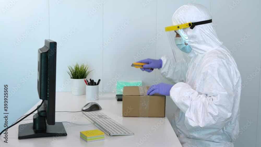 4K, Doctor in protective suit and plastic face shield opens a box and ...