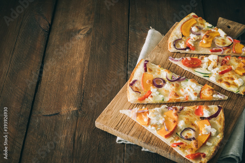 Pieces of tarte flambee with pumpkin, red onions and cheese on a rustic wooden table with copy space photo